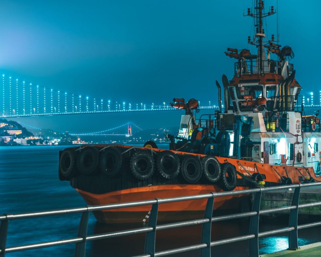 A tugboat parked along the Bosphorus Strait with the Bosphorus Bridge lit up in the background.