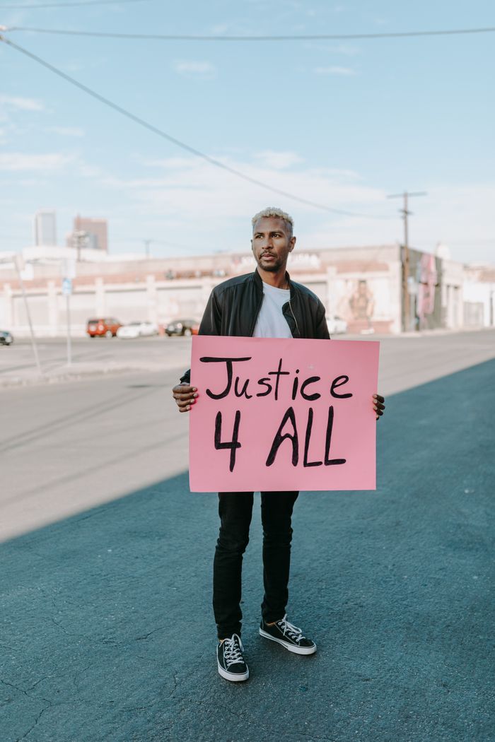 Man holds 'Justice 4 All' sign during a peaceful outdoor protest.